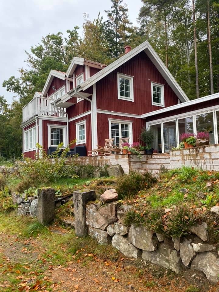 Röd villa med vita knutar och altan, höstlöv och stenmur