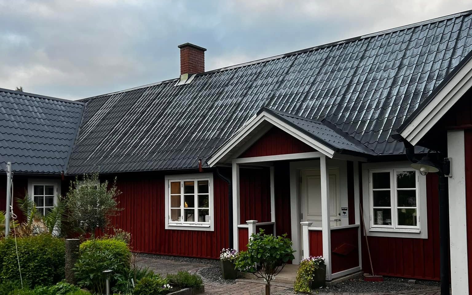 Röd gård med nymålat svart plåttak och stenlagd gårdsplan