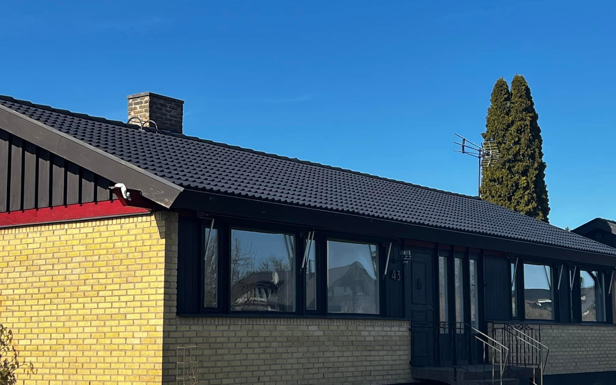 Villa i gult tegel med nymålat svart tak mot klarblå himmel