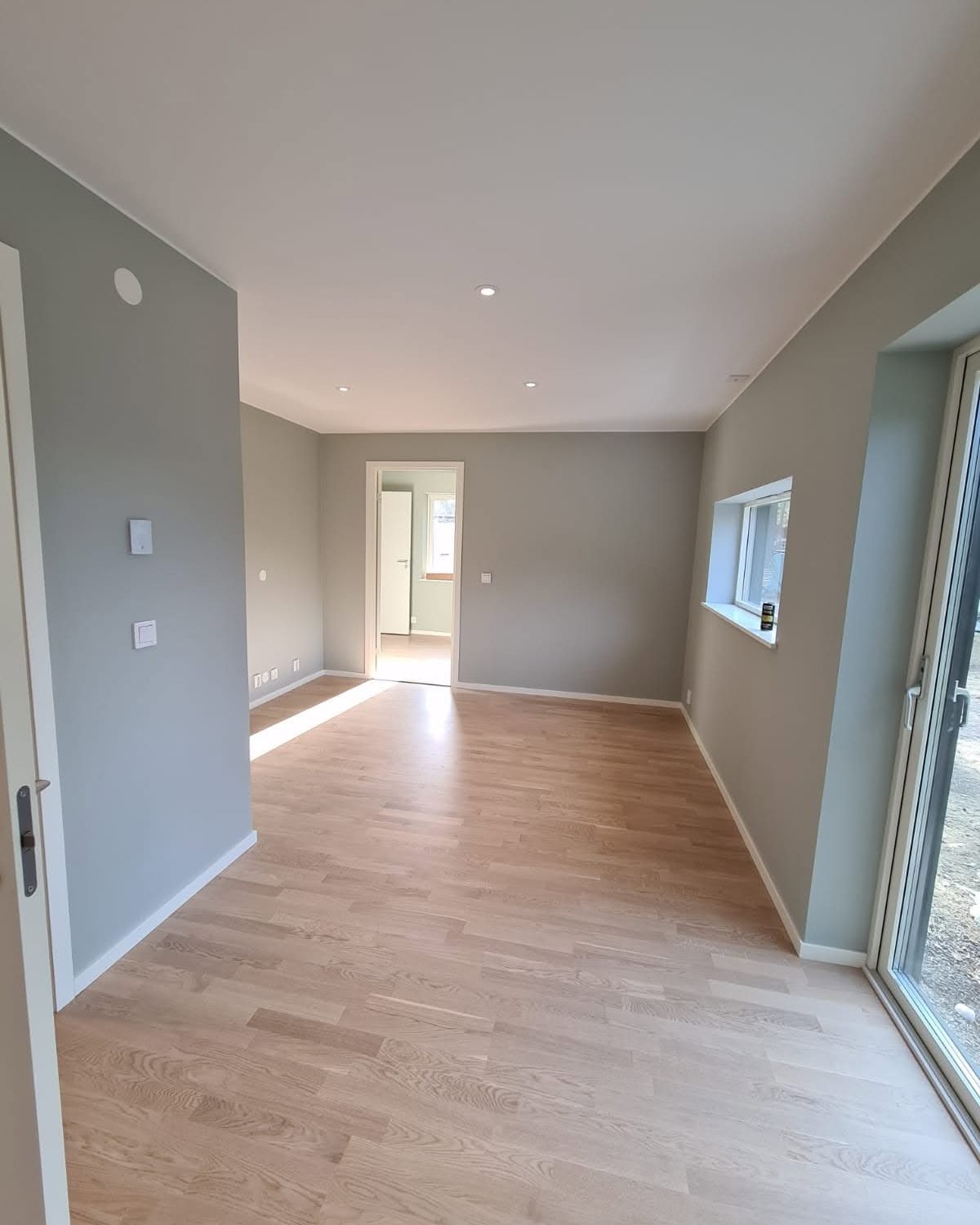 Nymålat vardagsrum med gråbeige väggar, vita tak och ekgolv