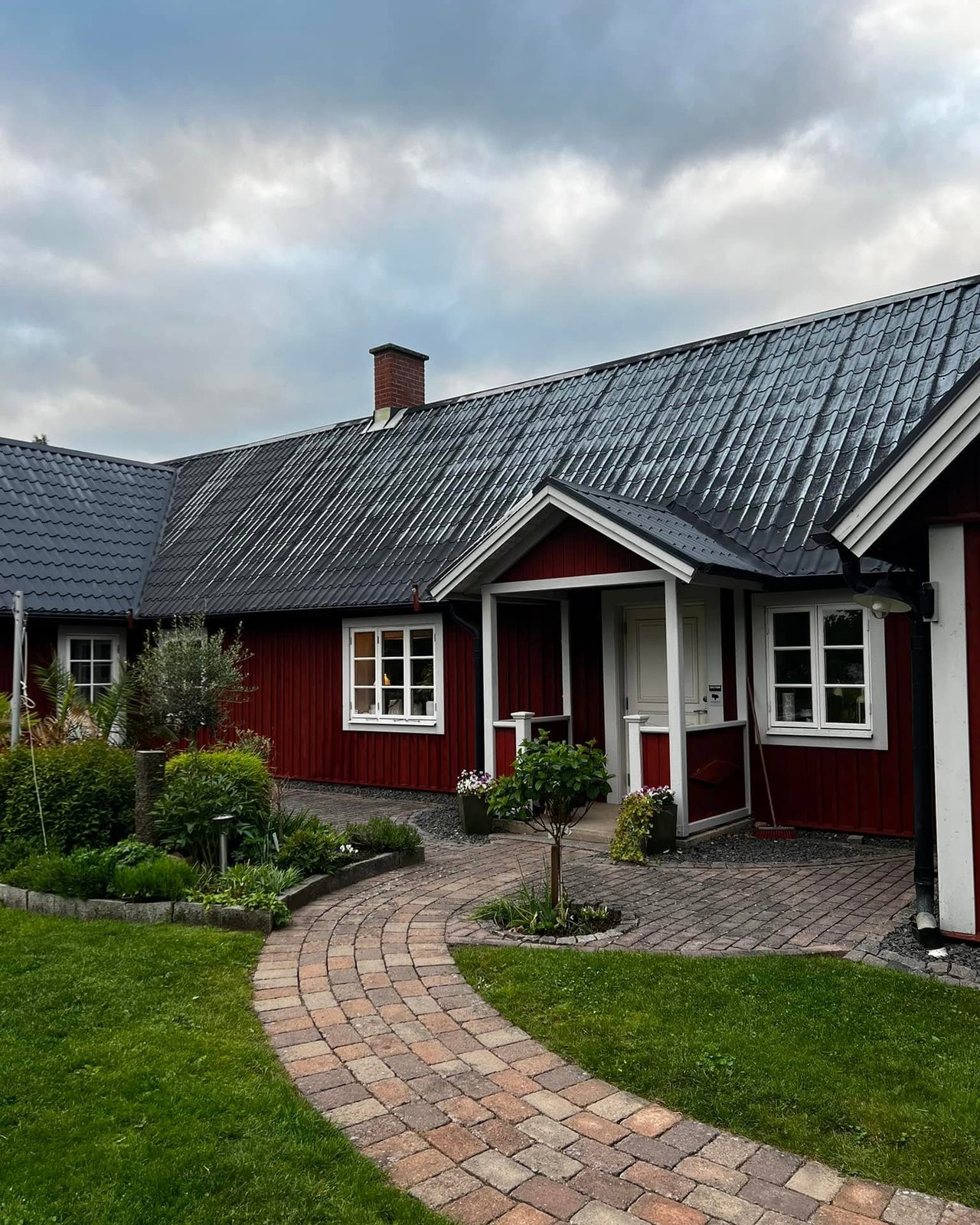 Röd gård med nymålat svart plåttak och stenlagd gårdsplan