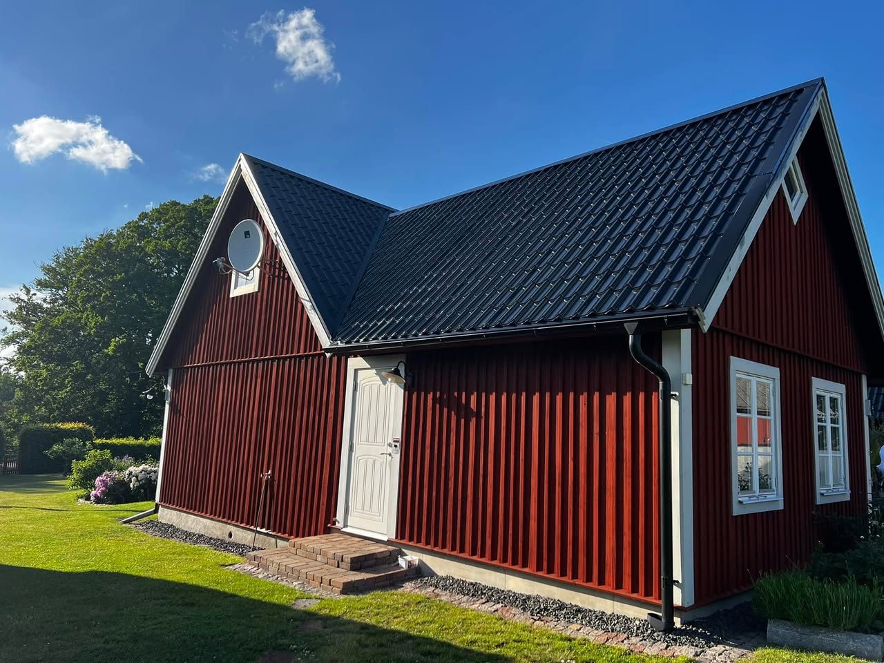 Rött hus med svart plåttak i solsken