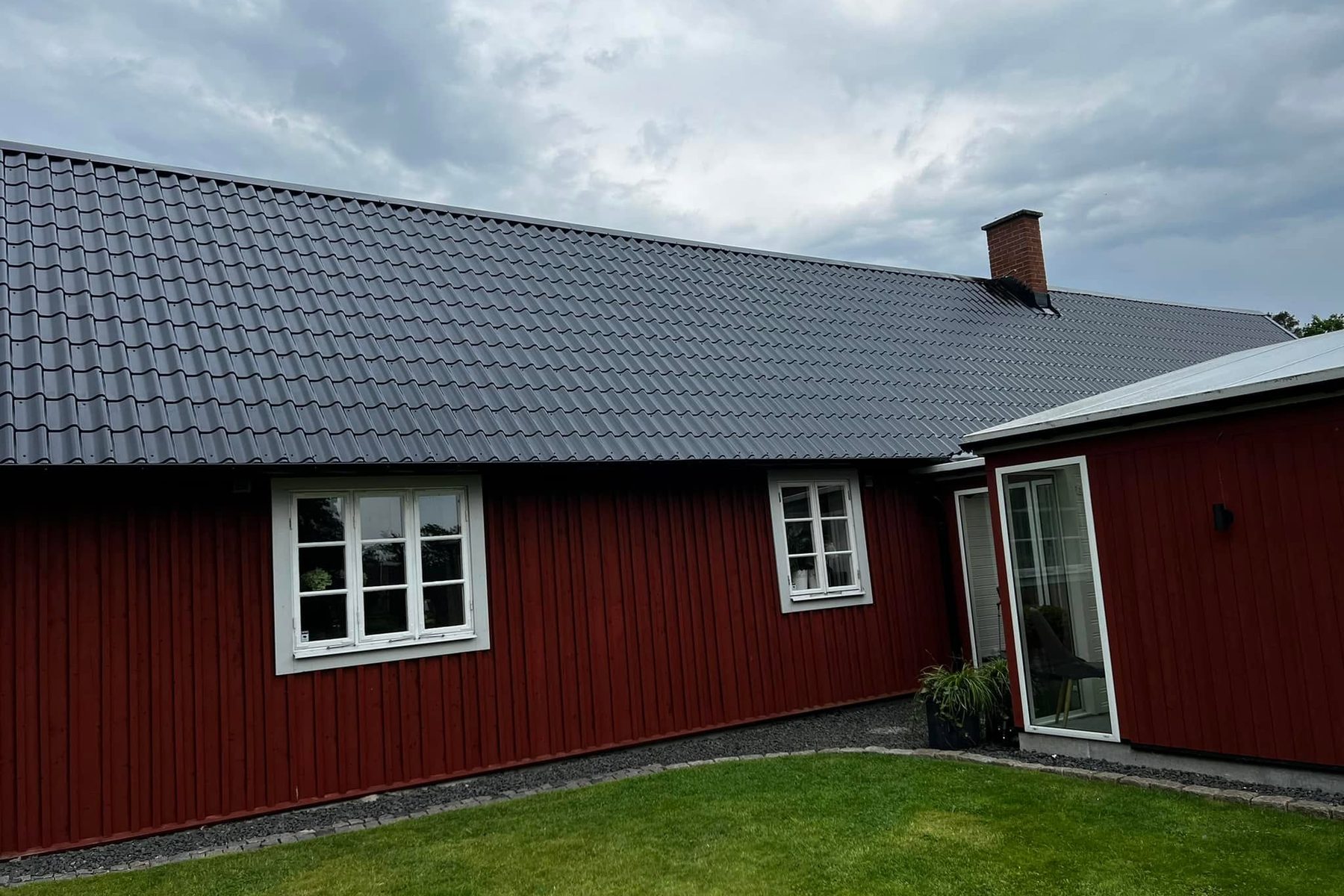 Röd länga med nymålat svart plåttak under molnig himmel